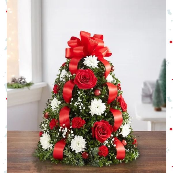 Árbol de Flores Navideñas Small. ¡El tradicional árbol favorito de las fiestas en donde empezó todo! Nuestro arreglo de árbol de flores es popular por su estética festiva y su tamaño compacto, que se adapta a cualquier entorno. Detalles del arreglo: Rosas Rojas y mini Claveles; Cojines blancos; Acentuado con baby’s breath, vegetación navideña variada, adornos y un lazo rojo en la parte superior. Domicilio Gratis Orlando FL, Fresh Flowers Orlando.