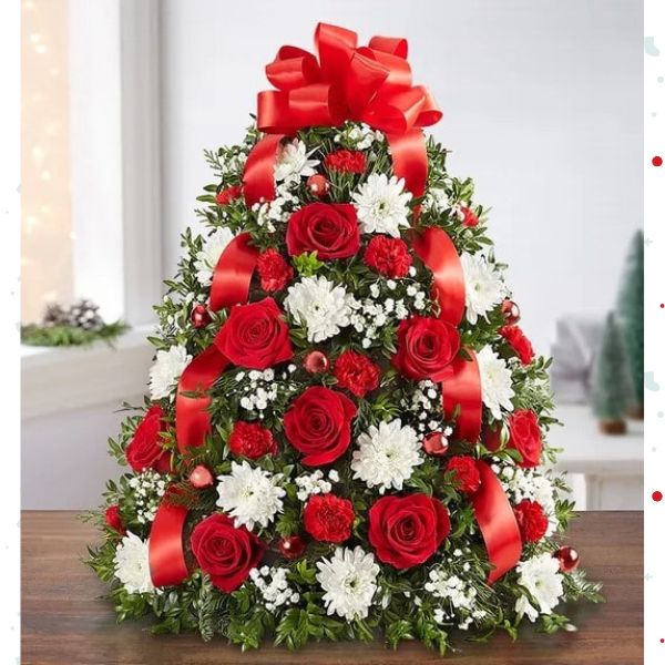 Árbol de Flores Navideñas Deluxe. ¡El tradicional árbol favorito de las fiestas en donde empezó todo! Nuestro arreglo de árbol de flores es popular por su estética festiva y su tamaño compacto, que se adapta a cualquier entorno. Detalles del arreglo: Rosas Rojas y mini Claveles; Cojines blancos; Acentuado con baby’s breath, vegetación navideña variada, adornos y un lazo rojo en la parte superior. Domicilio Gratis Orlando FL, Fresh Flowers Orlando.