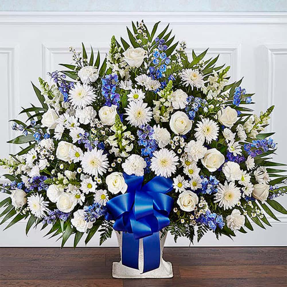 Sympathy Canasta De Piso, Size Extra Large, Fresh Flowers Orlando. Floor basket arrangement of blue delphinium; white roses, snapdragons, cremones, carnations, daisy poms and monte casino; accented with soft, lush greenery. Arreglo de canasta de piso con blue delphinium; rosas blancas, dragones, cremonas, claveles, margaritas y monte casino; decorado con vegetación en tonos verdes suaves.