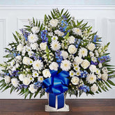 Sympathy Canasta De Piso, Size Extra Large, Fresh Flowers Orlando. Floor basket arrangement of blue delphinium; white roses, snapdragons, cremones, carnations, daisy poms and monte casino; accented with soft, lush greenery. Arreglo de canasta de piso con blue delphinium; rosas blancas, dragones, cremonas, claveles, margaritas y monte casino; decorado con vegetación en tonos verdes suaves.