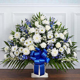 Sympathy Canasta De Piso, Size Large, Fresh Flowers Orlando. Floor basket arrangement of blue delphinium; white roses, snapdragons, cremones, carnations, daisy poms and monte casino; accented with soft, lush greenery. Arreglo de canasta de piso con blue delphinium; rosas blancas, dragones, cremonas, claveles, margaritas y monte casino; decorado con vegetación en tonos verdes suaves.