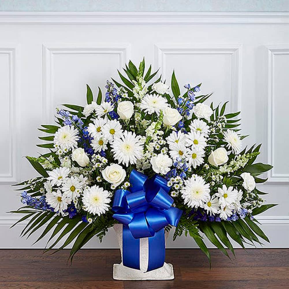 Sympathy Canasta De Piso, Size Medium, Fresh Flowers Orlando. Floor basket arrangement of blue delphinium; white roses, snapdragons, cremones, carnations, daisy poms and monte casino; accented with soft, lush greenery. Arreglo de canasta de piso con blue delphinium; rosas blancas, dragones, cremonas, claveles, margaritas y monte casino; decorado con vegetación en tonos verdes suaves.