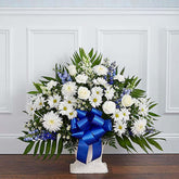 Sympathy Canasta De Piso, Size Small, Fresh Flowers Orlando. Floor basket arrangement of blue delphinium; white roses, snapdragons, cremones, carnations, daisy poms and monte casino; accented with soft, lush greenery. Arreglo de canasta de piso con blue delphinium; rosas blancas, dragones, cremonas, claveles, margaritas y monte casino; decorado con vegetación en tonos verdes suaves.