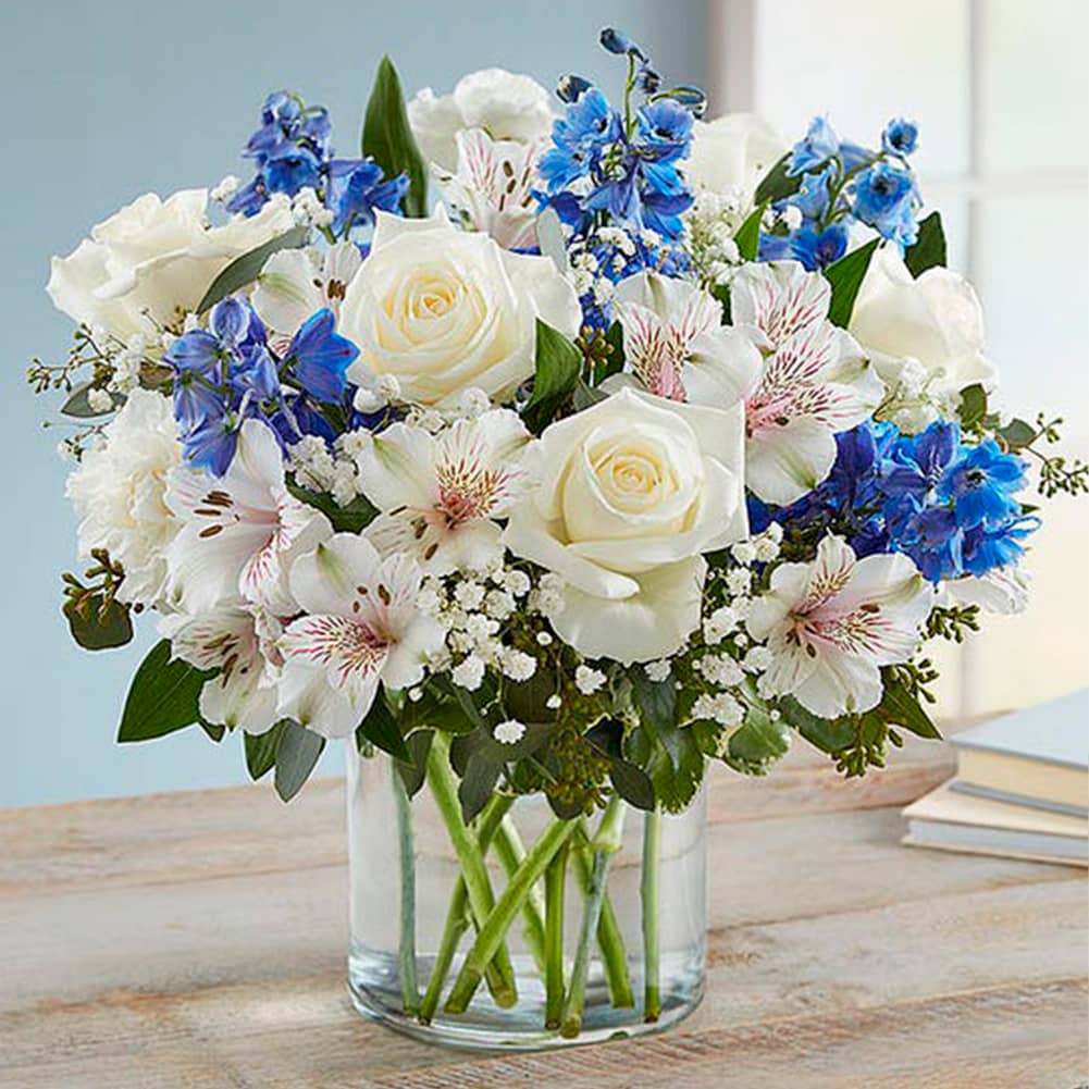 Sympathy Sentimientos Azul y Blanco, Size Large, Fresh Flowers Orlando. All-around arrangement with white roses, carnations, and Peruvian lilies (alstroemeria); blue delphinium; baby’s breath; seeded eucalyptus, and assorted greenery Peruvian lilies may arrive in bud form and will open to full beauty in 2-3 days. Arreglo completo con rosas blancas, claveles y lirios peruanos (alstroemeria); espuela de caballero azul; la respiración del bebé; eucalipto sin semillas y vegetación variada.