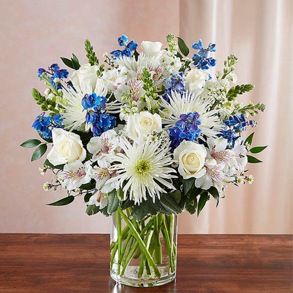 Sympathy Sincero Azul y Blanco, Size Small, Fresh Flowers Orlando. Our bountiful, heavenly blue and white bouquet features a soothing mix of blue delphinium, alstroemeria, and white roses, hand-designed inside a classic clear glass vase. When sent to a service or to the home of family or friends, it makes a genuinely heartwarming gesture. Nuestro ramo de flores en azul y blanco presenta una relajante mezcla de blue delphinium, alstroemeria y rosas blancas.
